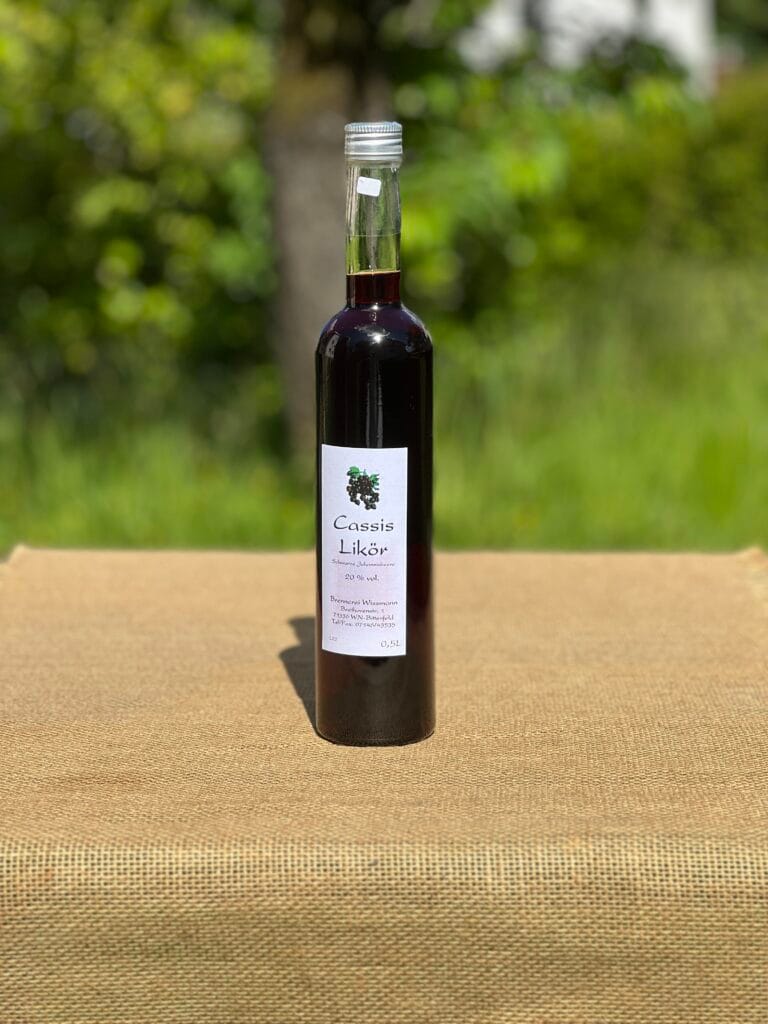 Eine Flasche Cassis-Lik&ouml;r auf einem Tisch mit idyllischem gr&uuml;nen Hintergrund.