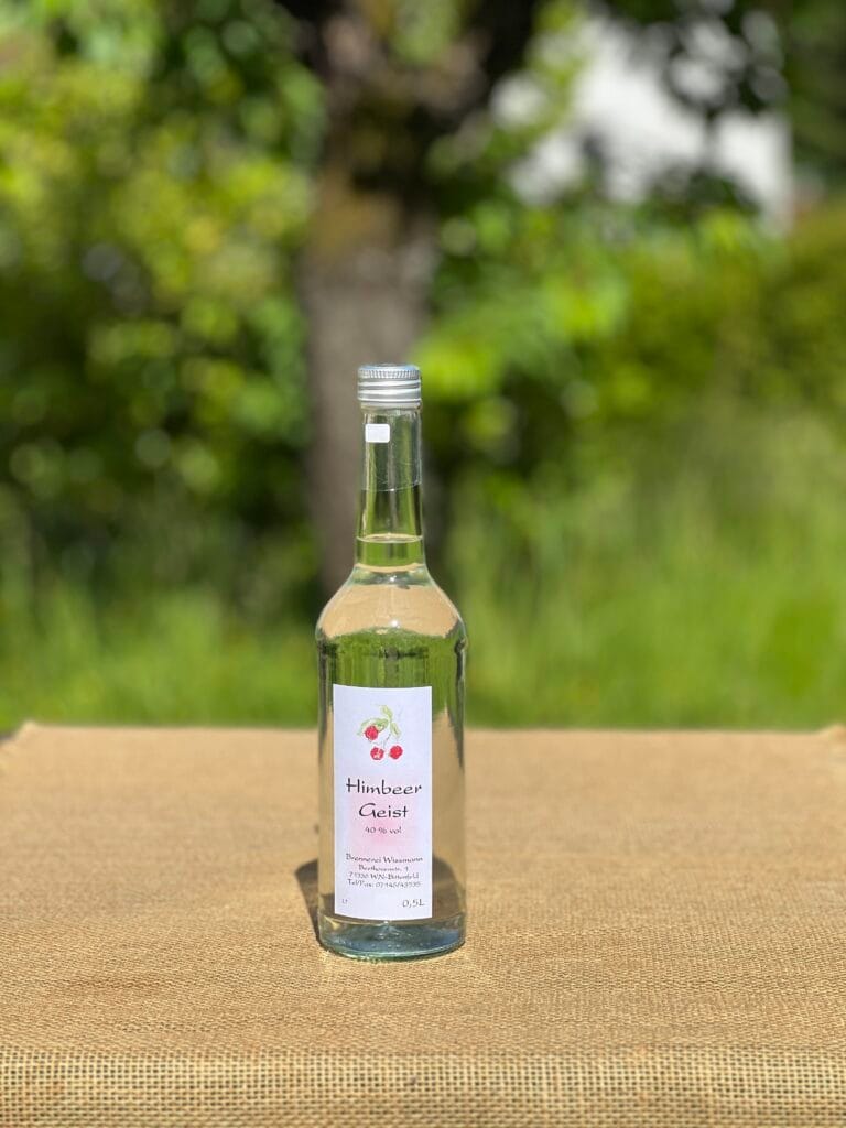 Eine Flasche Himbeergeist auf einem Tisch mit idyllischem gr&uuml;nen Hintergrund.