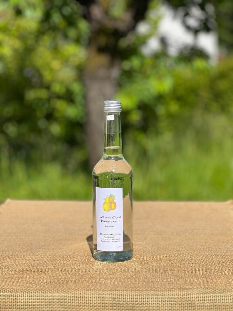 Eine Flasche Williams-Christ- Birnenbrand auf einem Tisch mit idyllischem gr&uuml;nen Hintergrund.