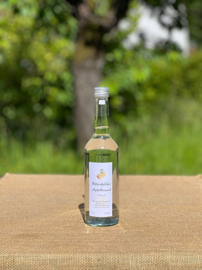 Eine Flasche Apfelbrand auf einem Tisch mit idyllischem gr&uuml;nen Hintergrund.