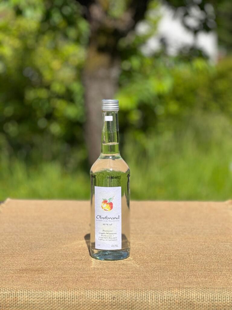Eine Flasche Obstbrand auf einem Tisch mit idyllischem gr&uuml;nen Hintergrund.