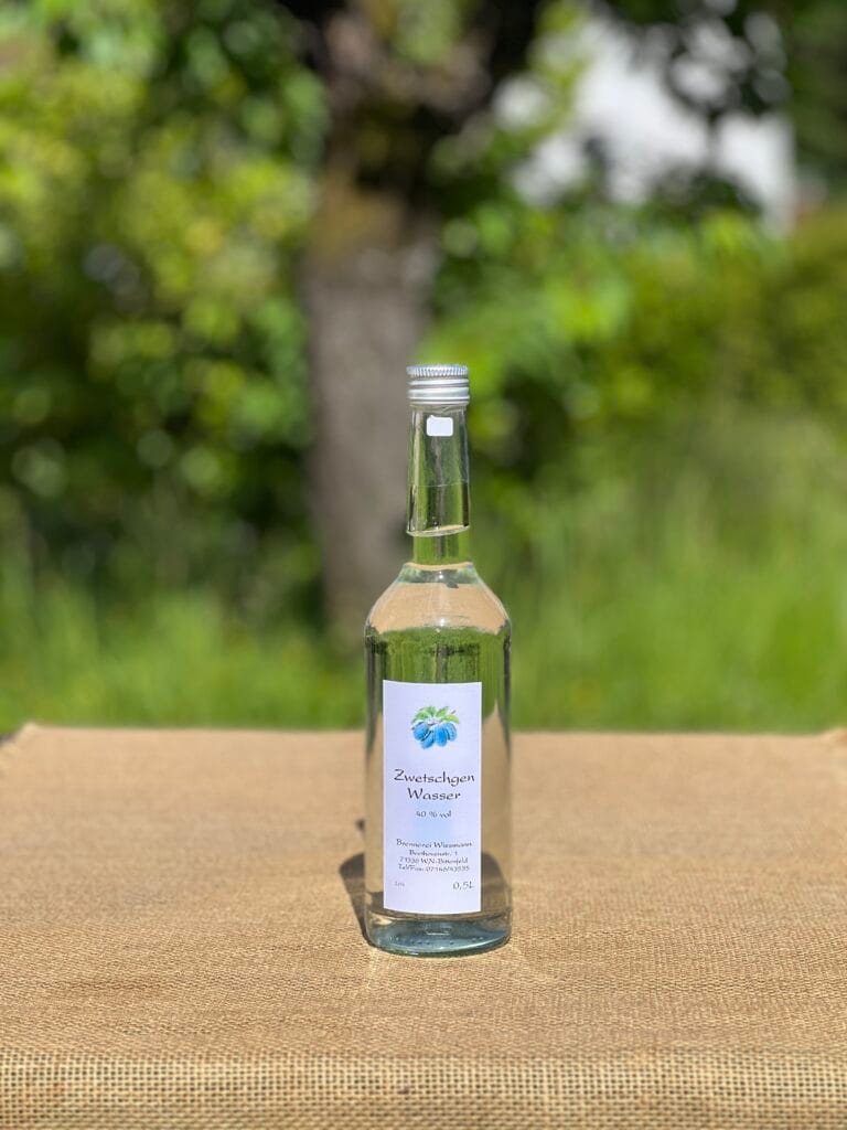Eine Flasche Zwetschgenwasser auf einem Tisch mit idyllischem gr&uuml;nen Hintergrund.