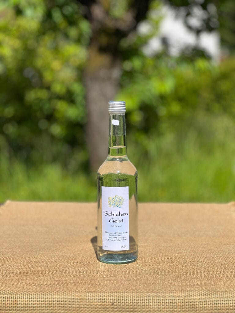Eine Flasche Schlehengeist auf einem Tisch mit idyllischem gr&uuml;nen Hintergrund.